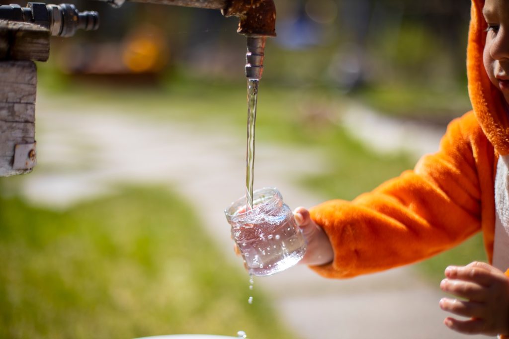 Faceless Little child fill bottle with water from water tap outdoors